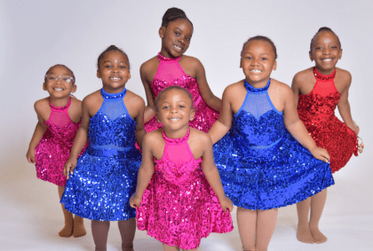 A group of young girls wearing colorful sequin dresses, smiling and enjoying a joyful moment together.